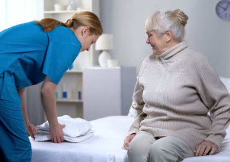 Nurse preparing clean bed-linen to elderly female patient