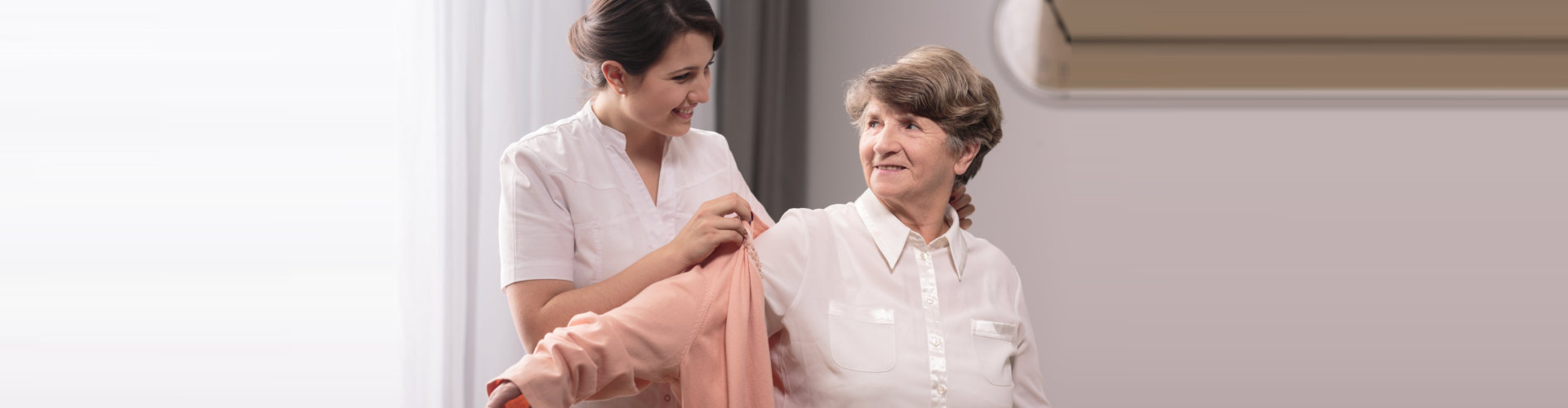 caregiver helping senior woman put on her clothes