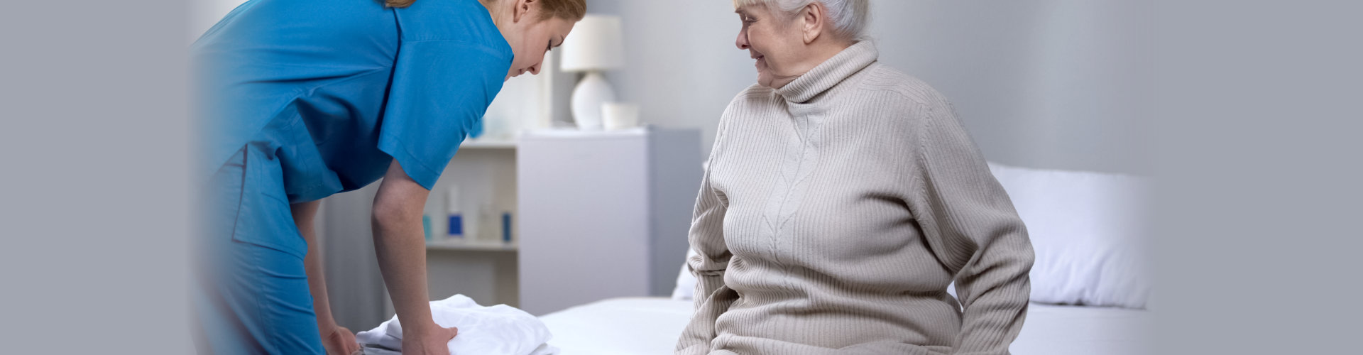 Nurse preparing clean bed-linen to elderly female patient